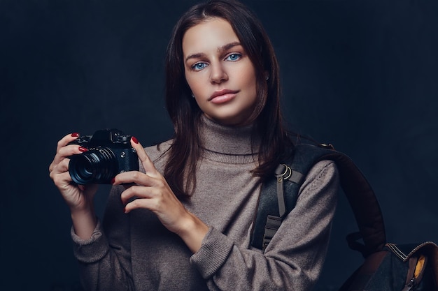 A brunette female traveler with backpack holds compact photo camera.