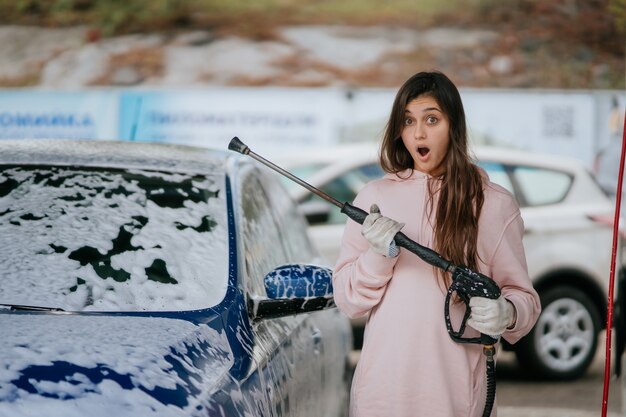 Brunette from a highpressure hose applies a cleaner on the car