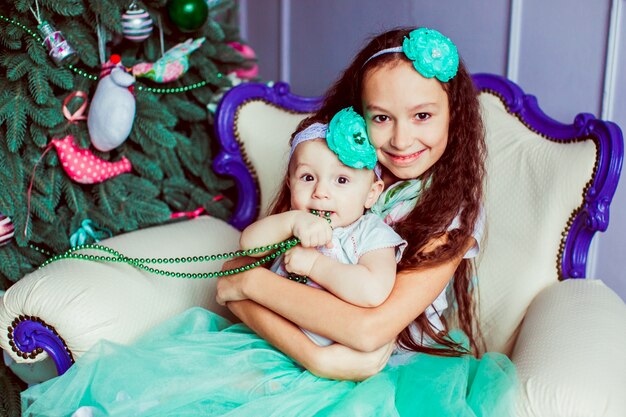 "Brunette girl embracing toddler sitting in chair"