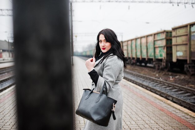 Brunette girl in gray coat posed in railway station