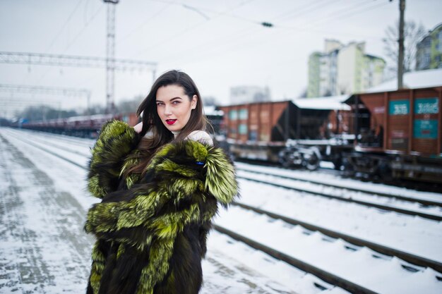 Brunette girl in green fur coat on the platform station at winter day