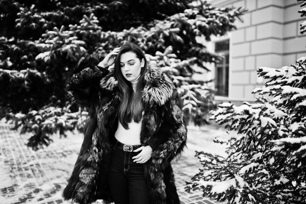 Brunette girl in green fur coat at winter day against snowy pine tree