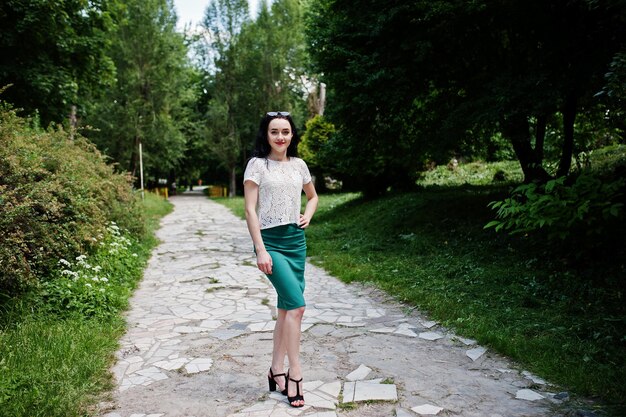 Brunette girl in green skirt and white blouse posed at park