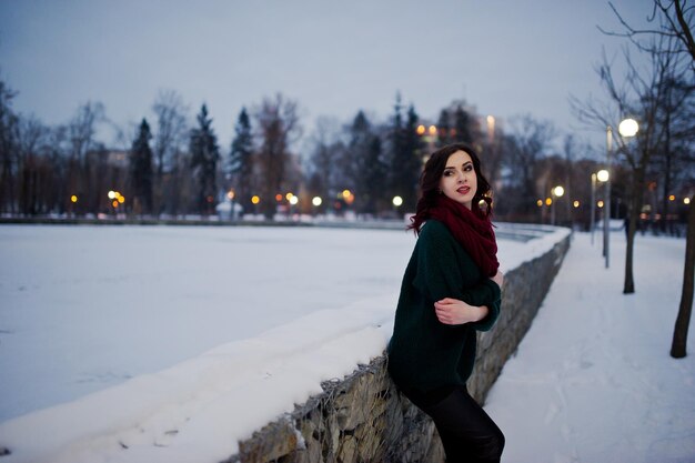 Brunette girl in green sweater and red scarf outdoor on evening winter day