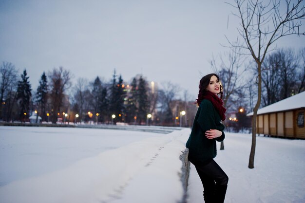 Brunette girl in green sweater and red scarf outdoor on evening winter day