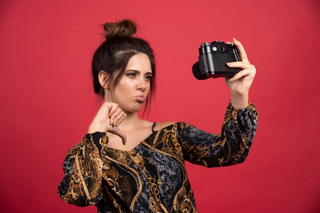 プロのデジタル一眼レフカメラを持っているブルネットの女の子は、彼女の失望した自分撮りを取ります。