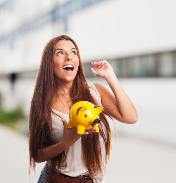 Brunette girl  holding yellow piglet moneybox