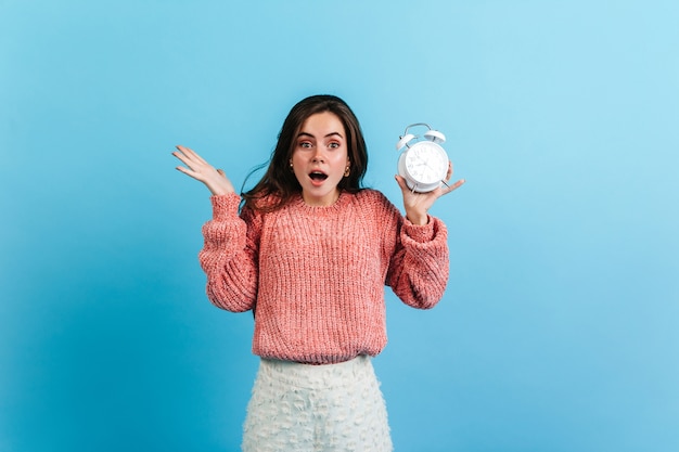 Free photo brunette girl keeps alarm clock on blue wall.