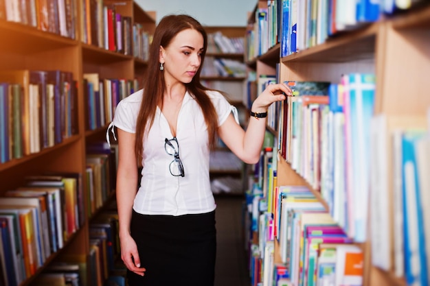 白いブラウスと黒いミニスカートに図書館でブルネットの女の子が着るセクシーなビジネスの女性や教師のコンセプト