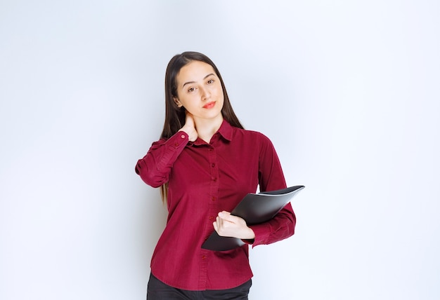 A brunette girl model standing and posing with a folder against white wall.