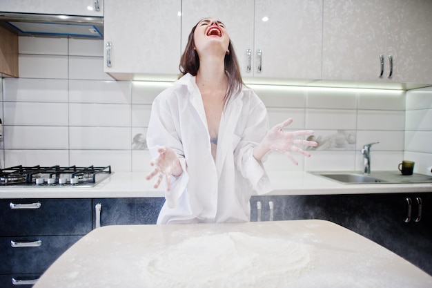 Brunette girl wear at shirt and underwear play with flour at the white kitchen