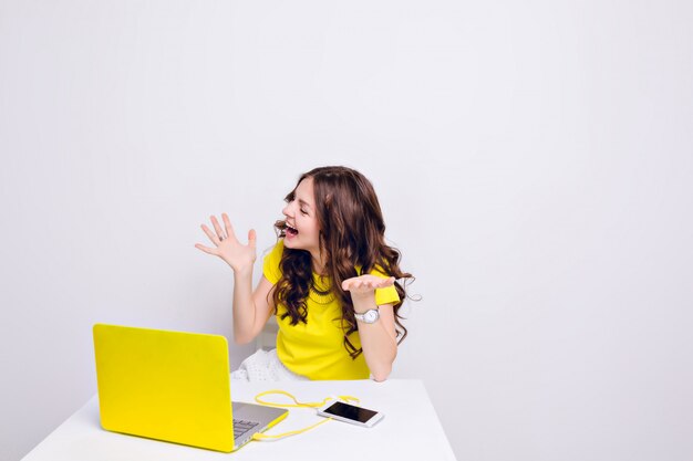 A brunette girl with curly hair is playing silly in front of a laptop in yellow case.