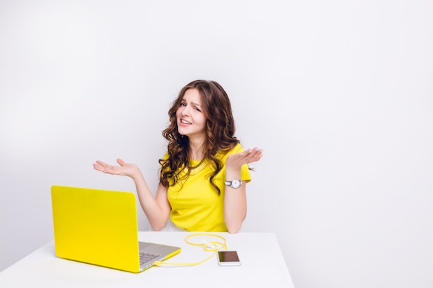A brunette girl with curly hair looks confused sitting in front of laptop in yellow case.