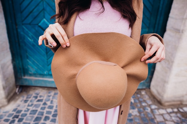 Brunette lady holds beige hat before her dress 