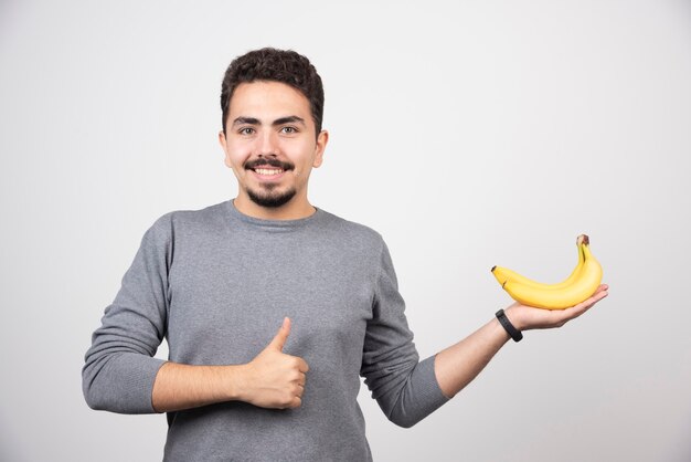 Brunette male holding banana and giving thumbs up.