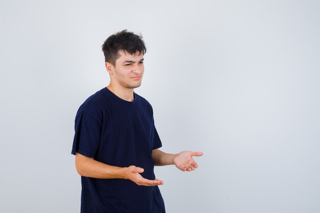 Brunette man in dark t-shirt making asking question gesture and looking unhappy .