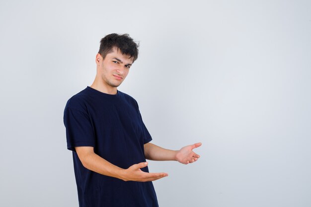 Brunette man in dark t-shirt stretching hands forward, standing sideways and looking displeased , front view.