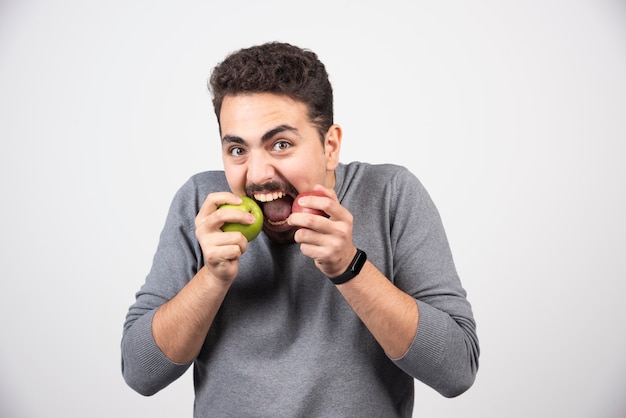 緑と赤のリンゴを食べるブルネットの男。