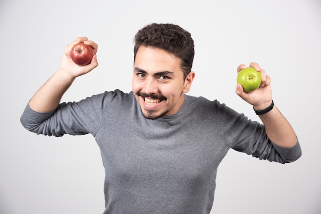 Brunette man holding green and red apples happily.