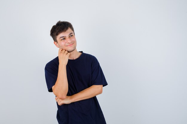 Brunette man holding hand on chin in t-shirt and looking pleased. front view.