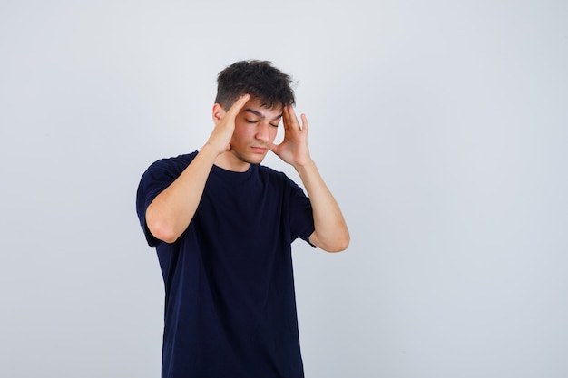 Brunette man holding hands on head in dark t-shirt and looking thoughtful.