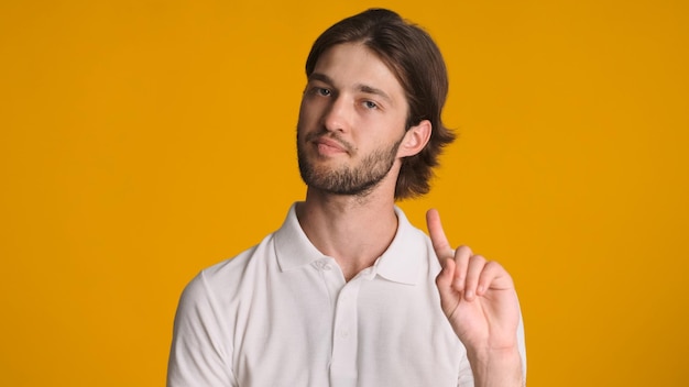 Brunette man looking confident showing no gesture at camera isolated on orange background Disagree expression