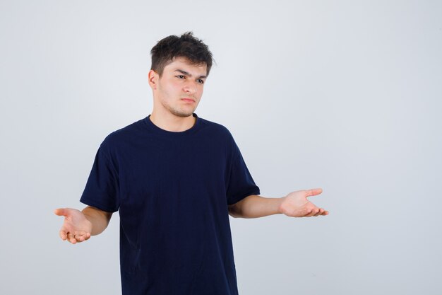 Brunette man making asking question gesture in dark t-shirt and looking disappointed , front view.