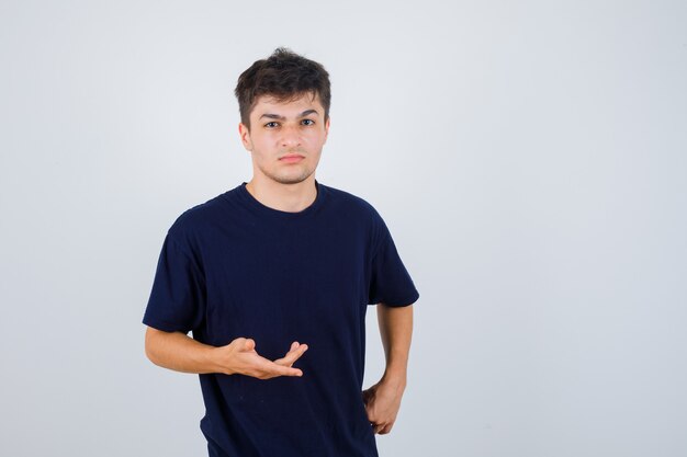 Brunette man making asking question gesture in dark t-shirt and looking wistful , front view.