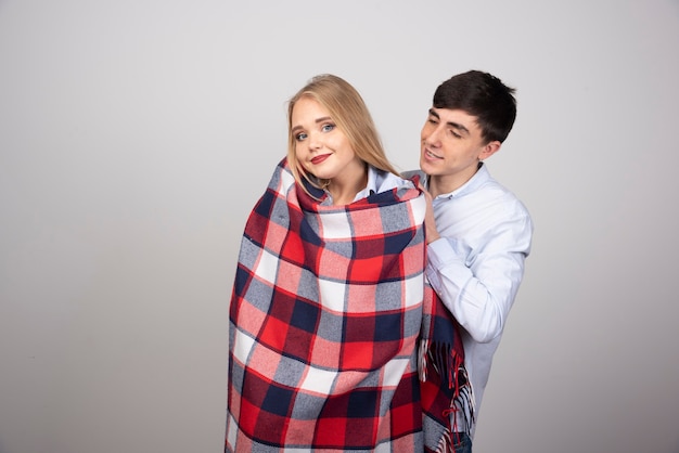 Brunette man model covering checkered blanket to blonde woman