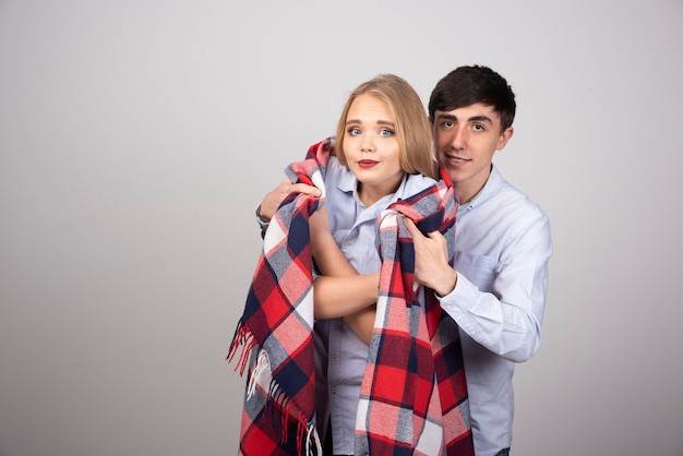 Brunette man model covering checkered blanket to blonde woman