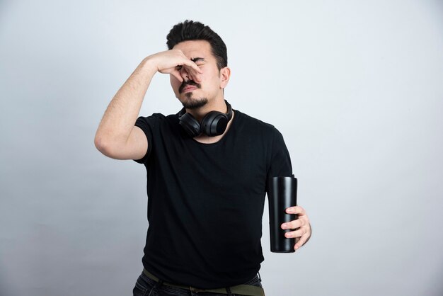 Brunette man model holding a cup and closing nose with disgust . 