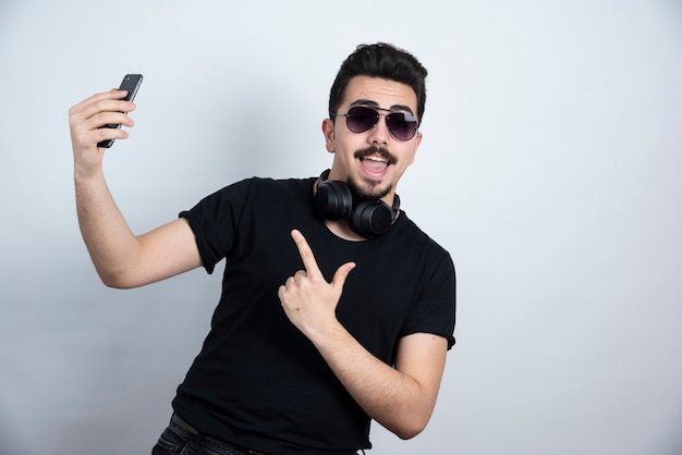 Brunette man model standing in headphones and holding mobile phone . 