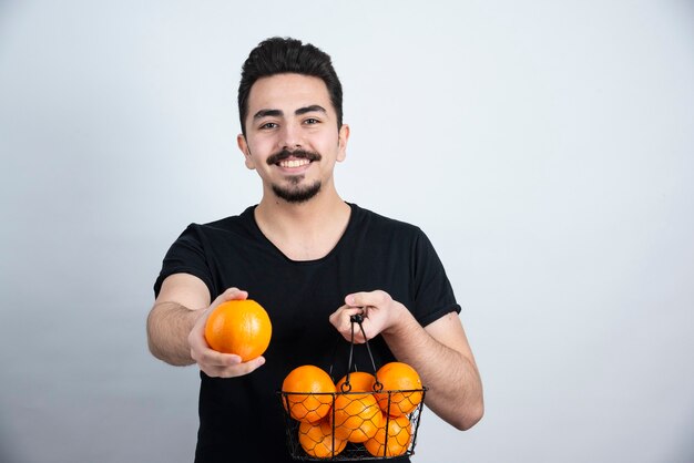 ブルネットの男性モデルが立って、オレンジ色の果物でポーズをとる。