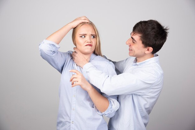 Brunette man model strangling blonde woman on gray background