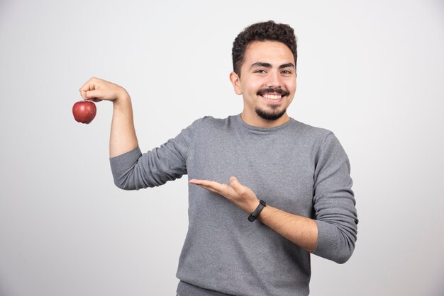 Brunette man pointing at red apple on gray.