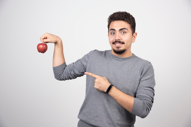 Brunette man pointing at red apple on gray.