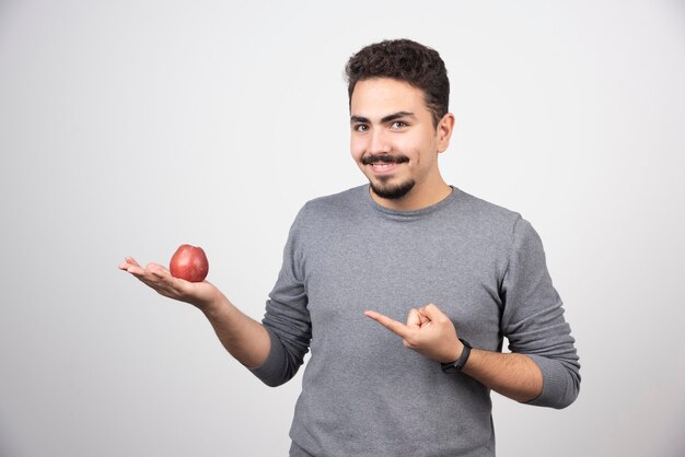 Brunette man pointing at red apple on gray.