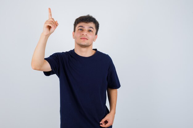 Brunette man pointing up in t-shirt and looking careful , front view.