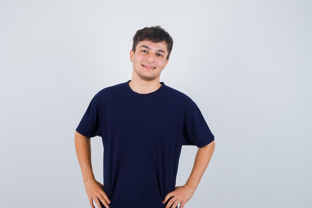 Brunette man posing with hands on waist in t-shirt and looking cheery. front view.