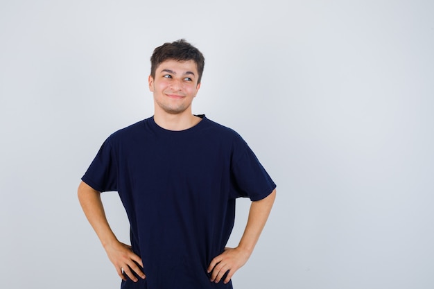 Brunette man posing with hands on waist in t-shirt and looking merry. front view.