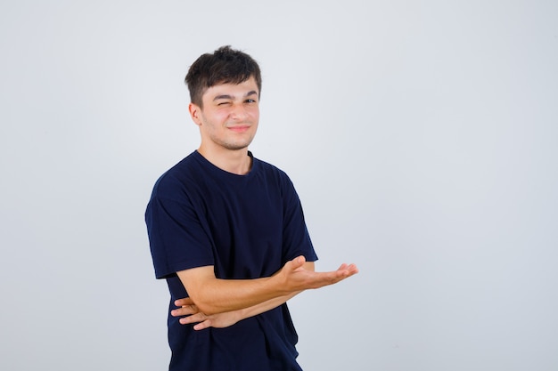 Brunette man pretending to show something in t-shirt and looking cheery. front view.