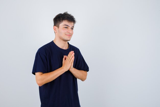 Brunette man showing namaste gesture in dark t-shirt and looking handsome .