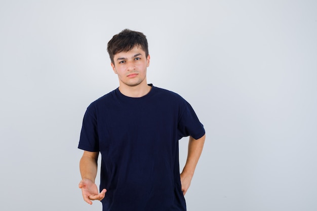 Brunette man stretching hand in questioning gesture in t-shirt and looking focused , front view.