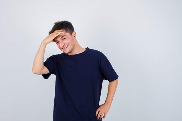 Brunette man in t-shirt holding hand over head and looking joyful , front view.