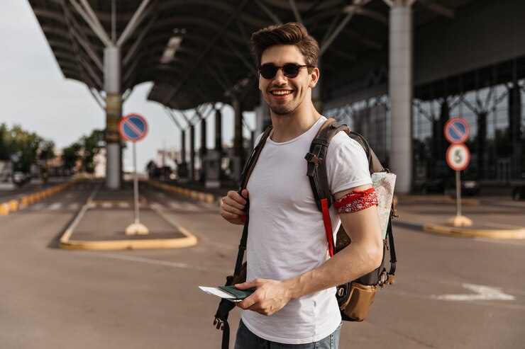 Free Photo brunette man traveler in white tee and sunglasses smiles near airport