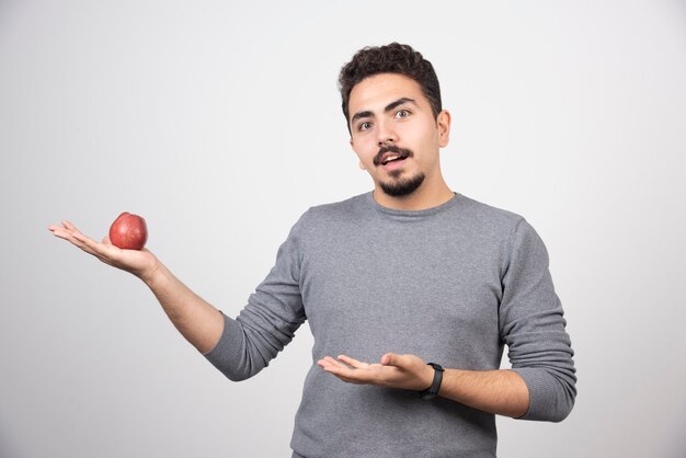 Brunette man with red apple looking at camera.