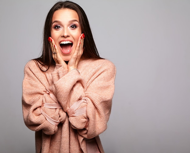 brunette model in casual beige warm sweater clothes on gray covering her face with hands