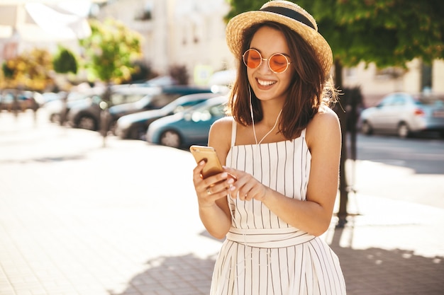 брюнетка модель в летней одежде позирует на улице с помощью мобильного телефона