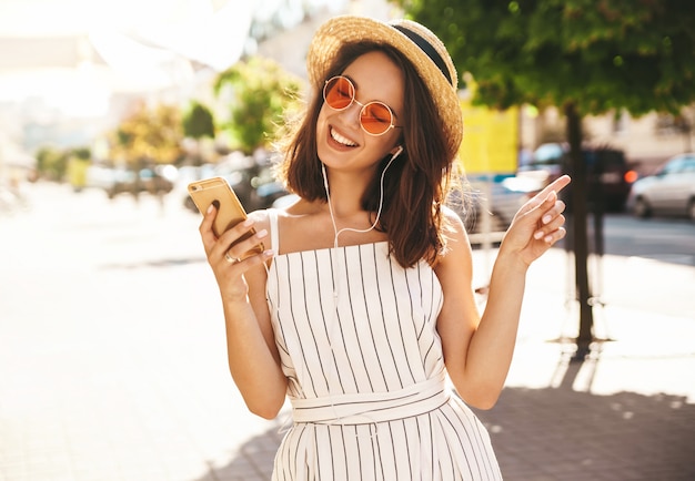 брюнетка модель в летней одежде позирует на улице с помощью мобильного телефона