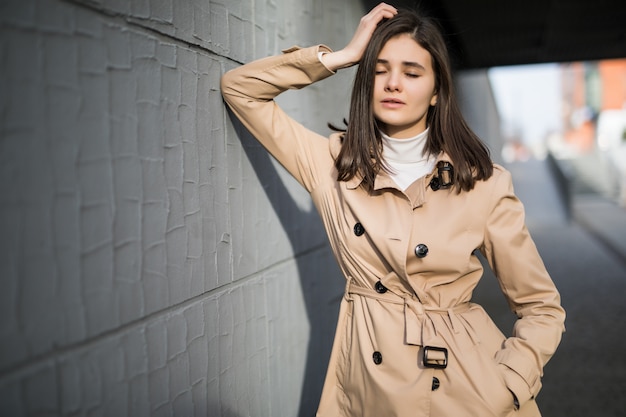 Brunette model with clothed eyes stays near grey wall outside